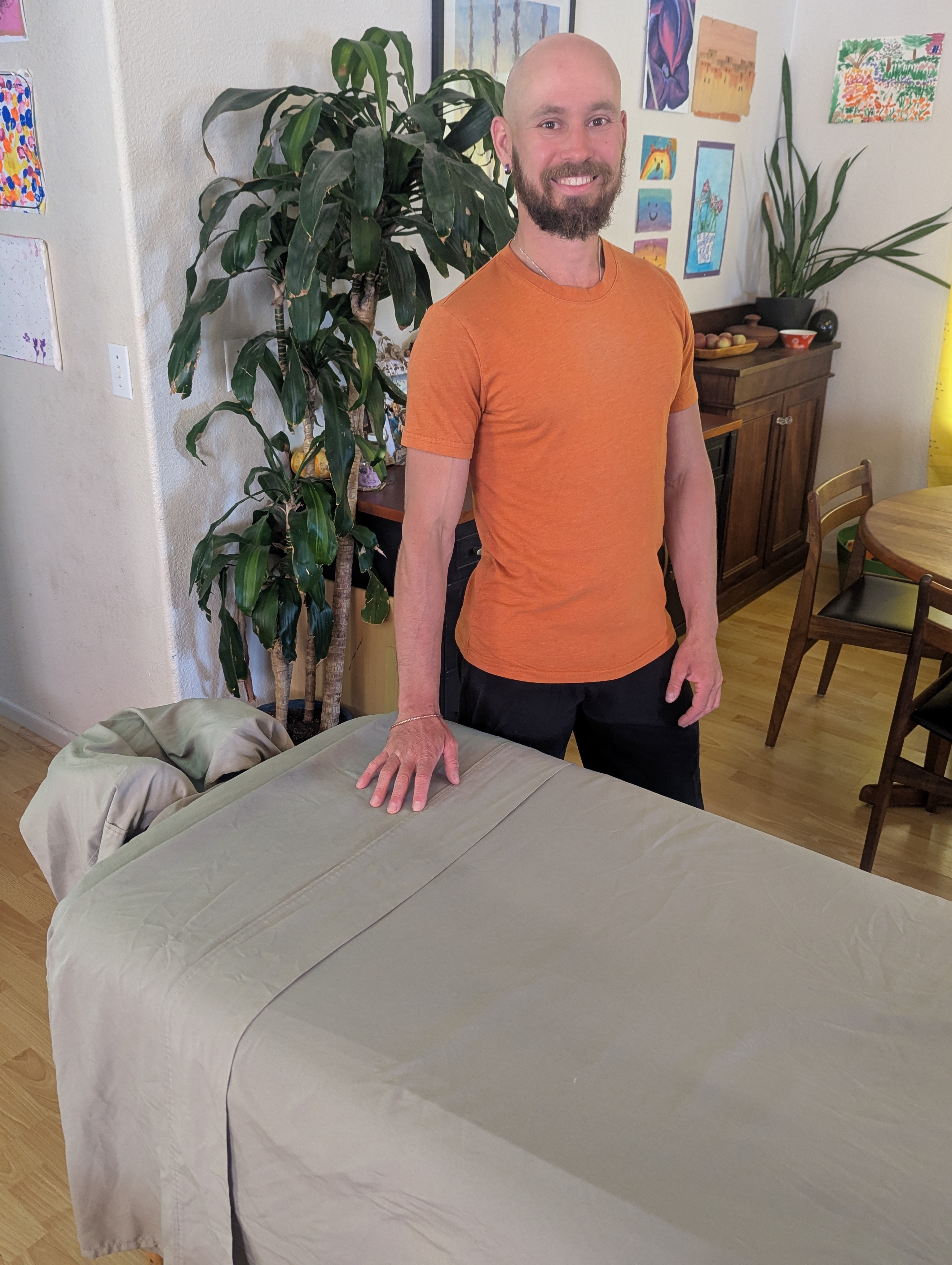 Tommy standing beside a prepared massage table in a warm, plant-filled room