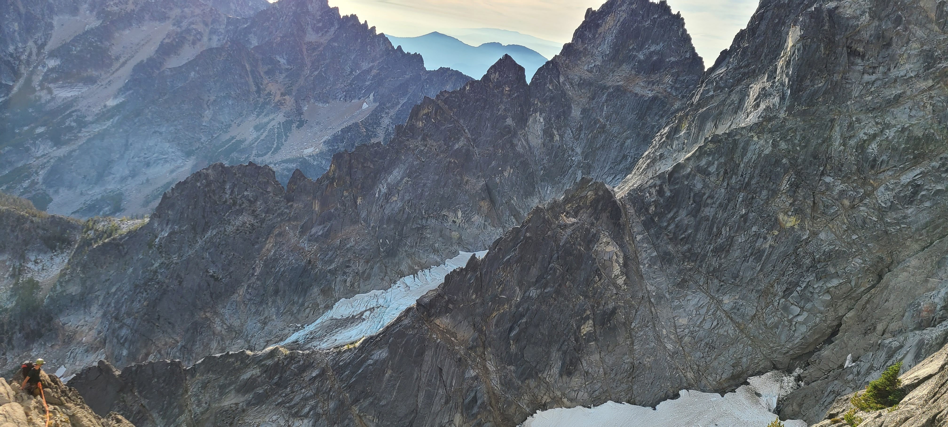 A climber moving along a rocky ridge above a glaciated mountain basin