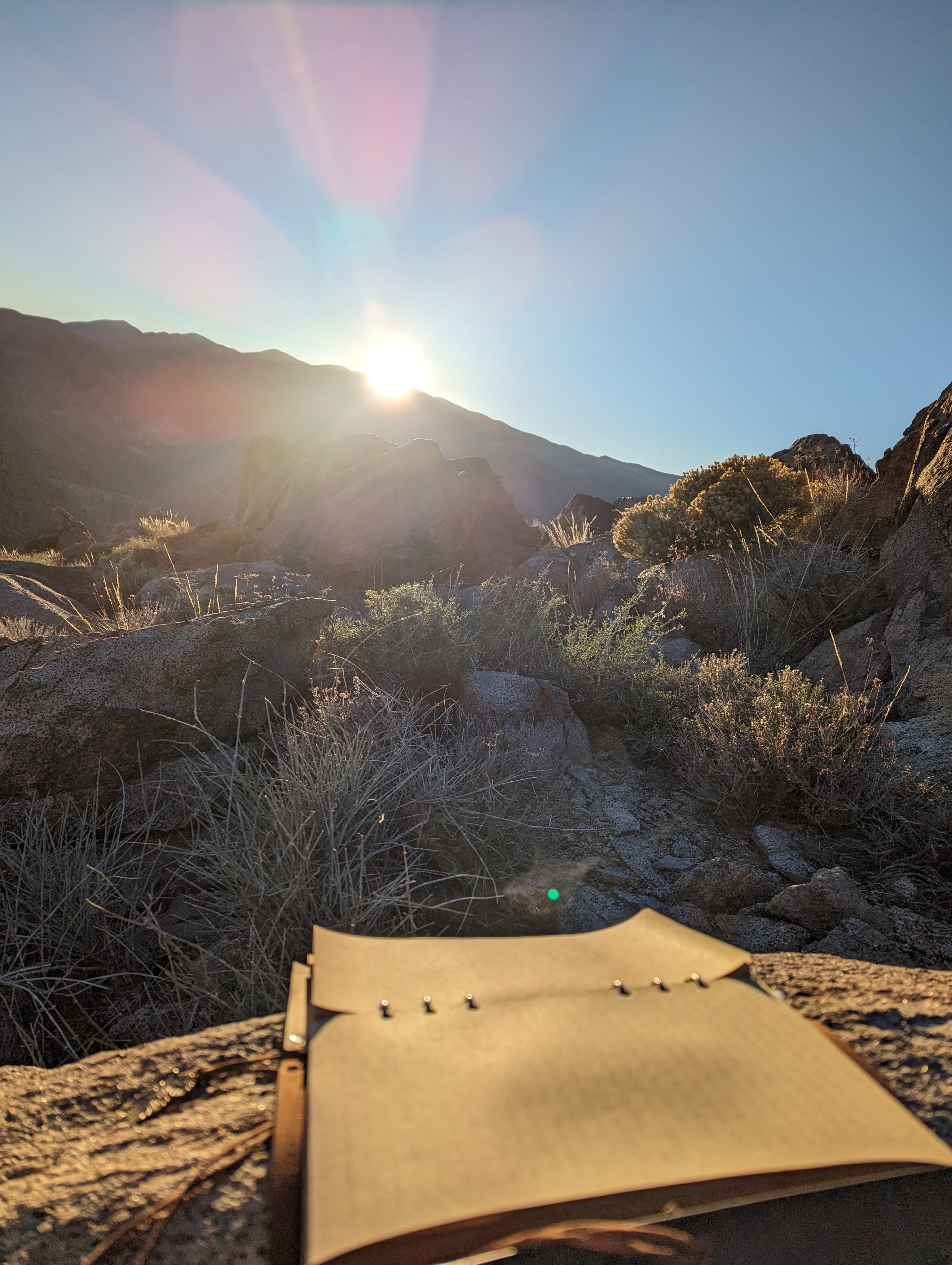 An open notebook resting on wood in a rocky landscape at sunset